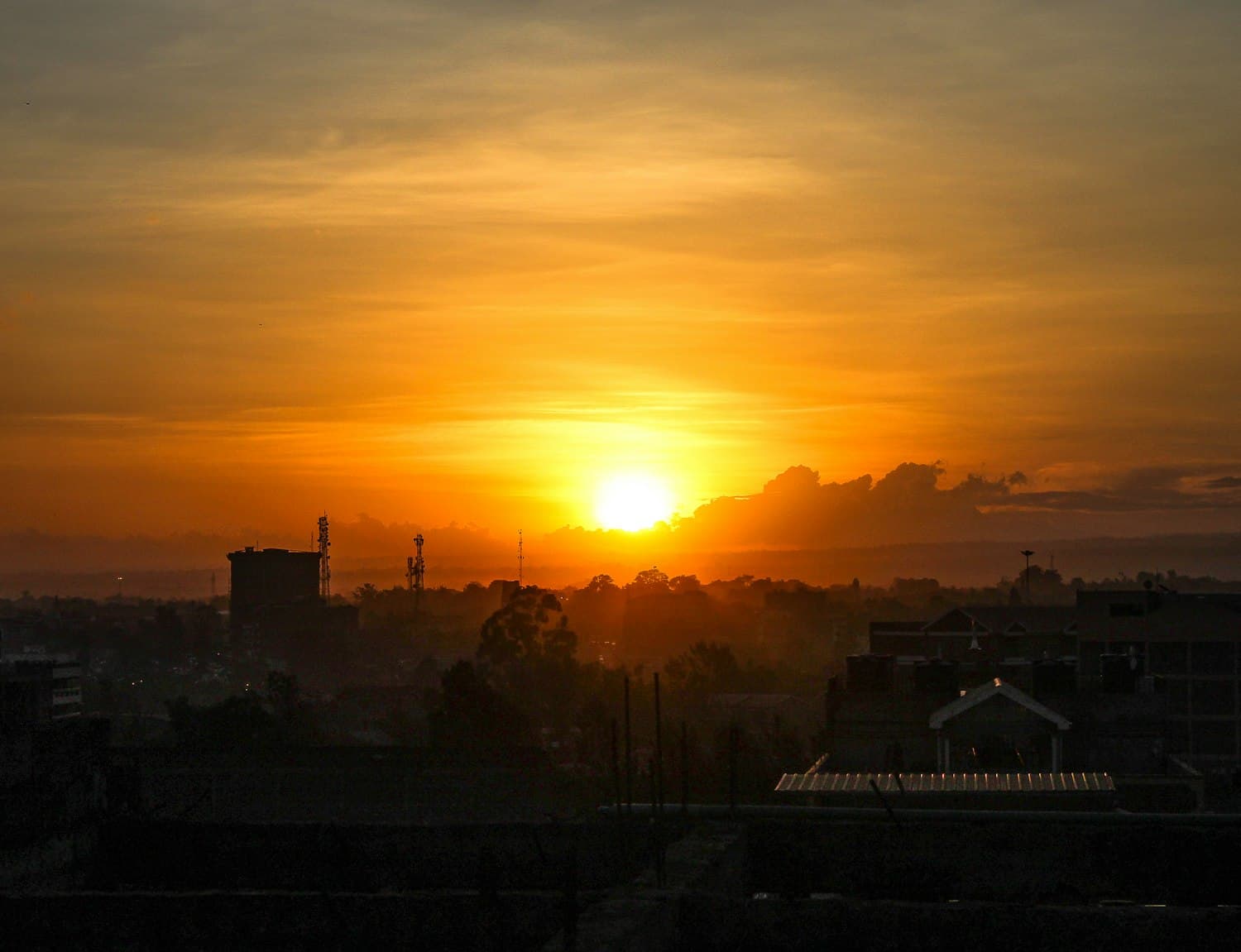 A hazy sun low over Atlanta, silhouetting low-rise rooftops and communication masts